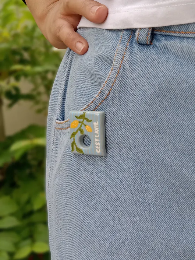 Studio Gayatri handmade botanical clay sunglasses holder brooch featuring a hand-painted blue and yellow lemon branch design.