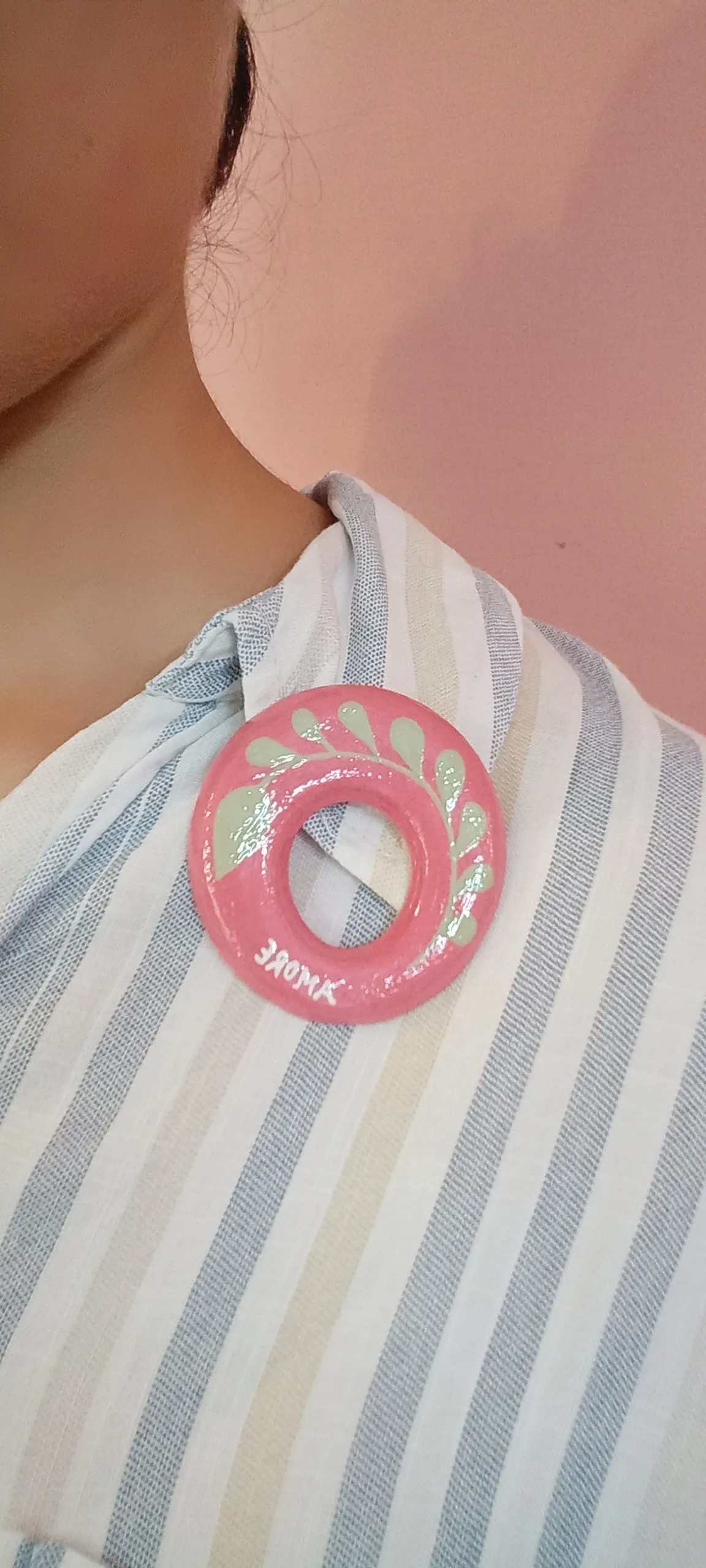 Oval clay pink brooch pin pinned to the collar of a cotton shirt