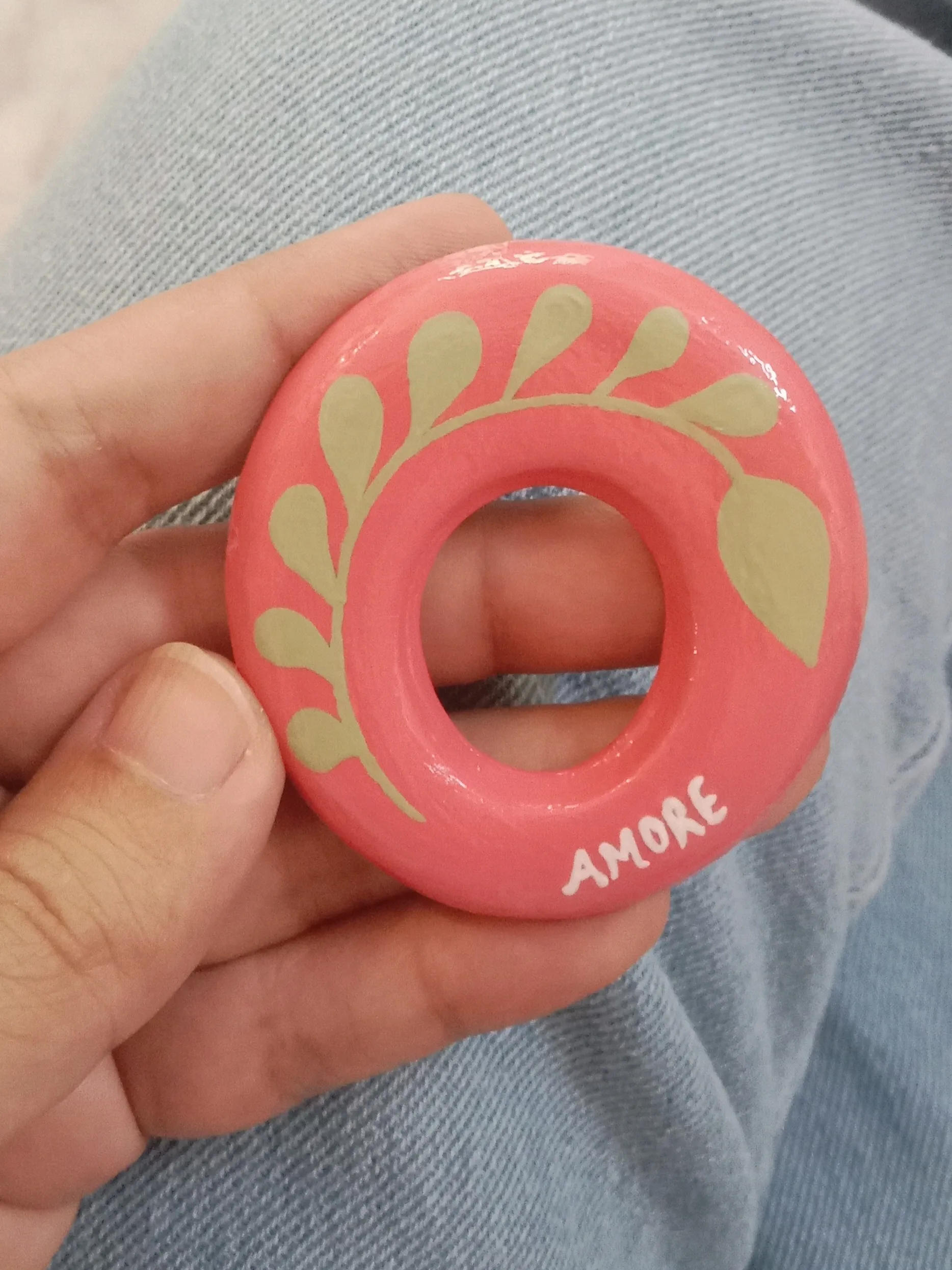 Close up of the hand-painted olive green leaf motif and high-gloss glaze finish on an oval pink clay eyeglass holding pin.